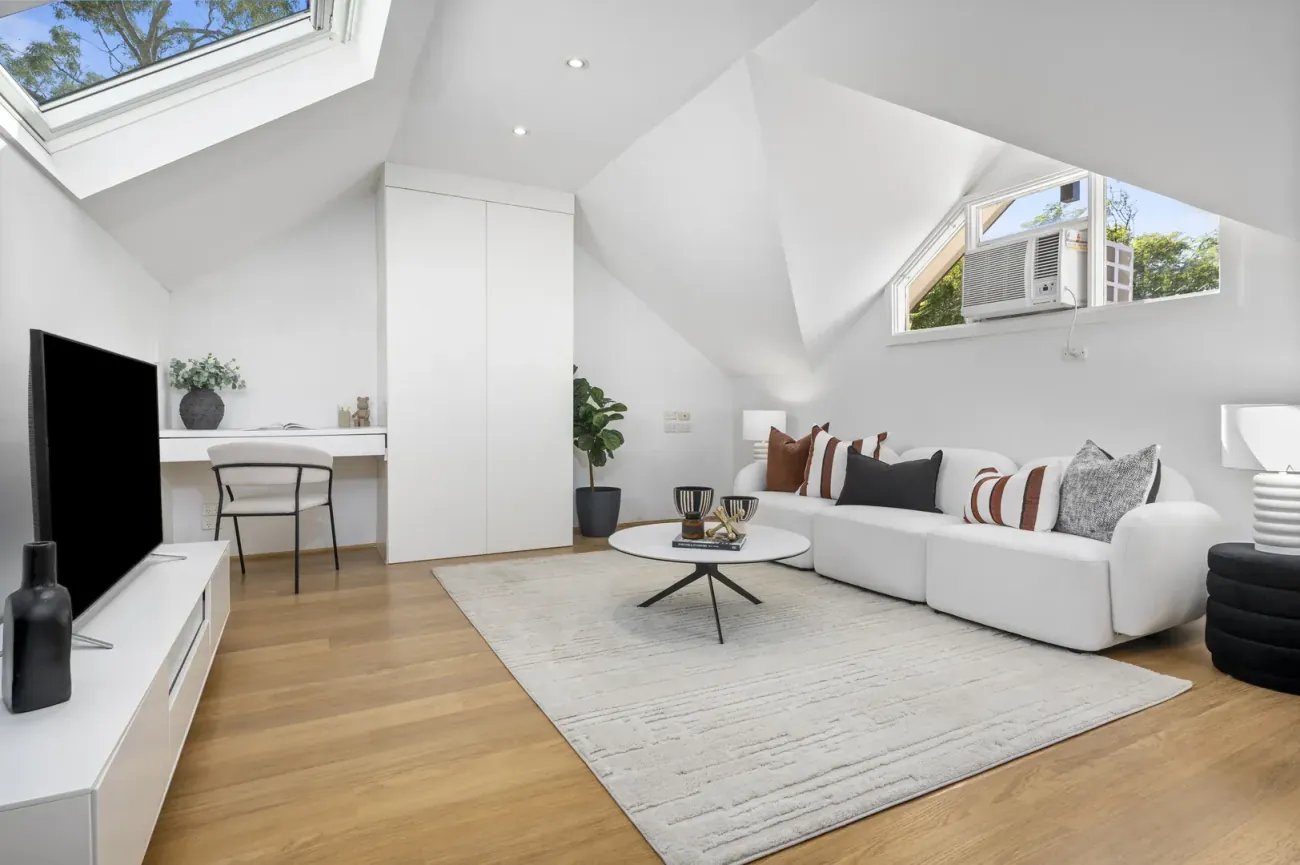 An attic-converted living room with a white modular sofa, black-and-rust pillows, and a small white coffee table.