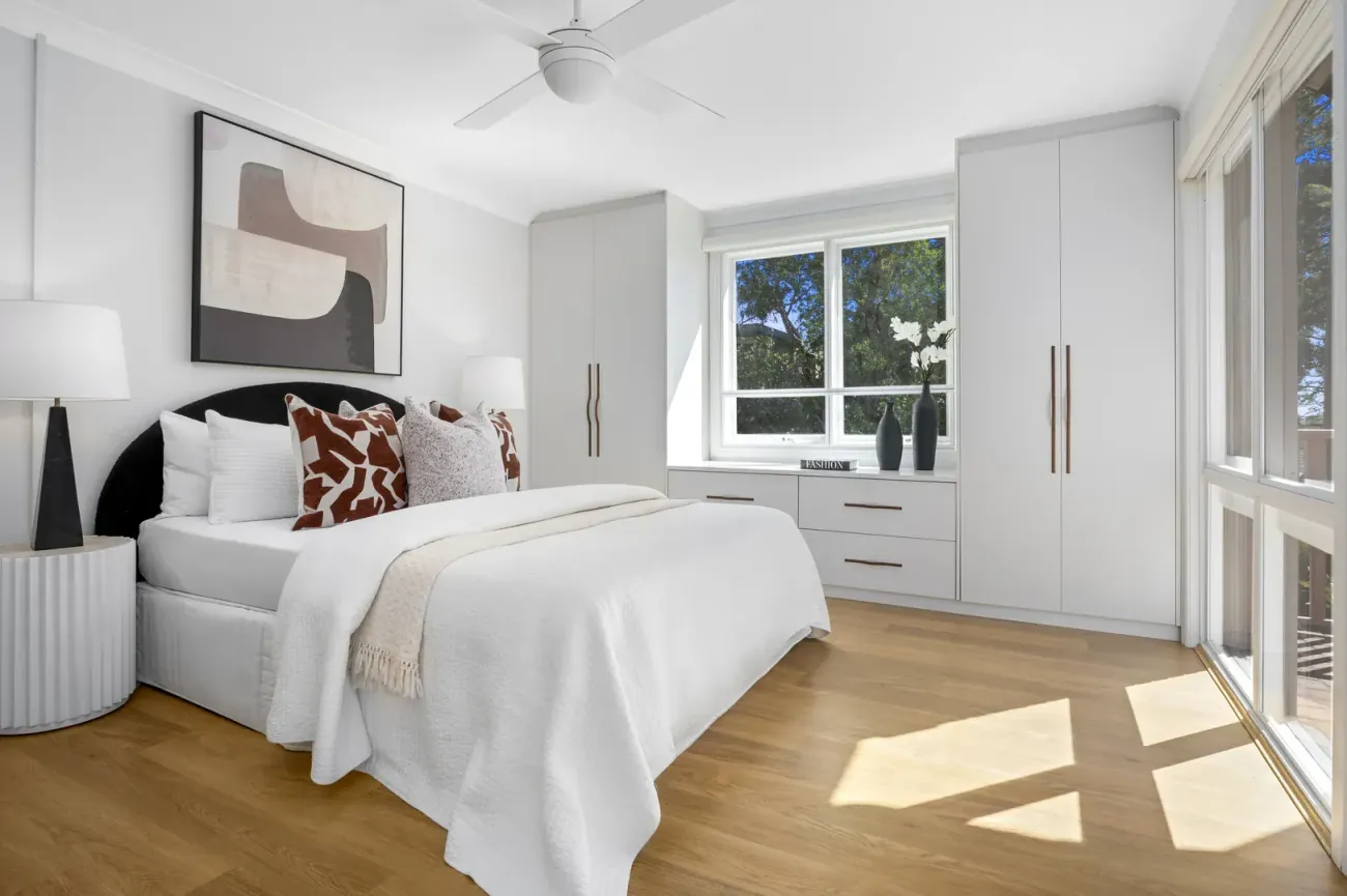 A plain bedroom with grey-and-rust pillows and an abstract artwork.
